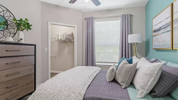 Bedroom with a queen bed, nightstand, dresser, hardwood-style flooring, large window, and walk-in closet.