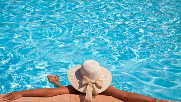 Woman relaxing at the edge of the pool with a large, white sunhat